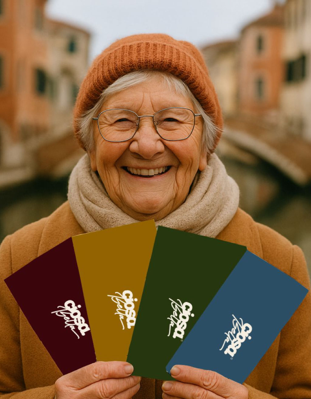Tombola Ciosota – Scartine colori 2026 Persona anziana sorridente tiene in mano quattro scartine colorate della Tombola Ciosota davanti a un canale di Chioggia.